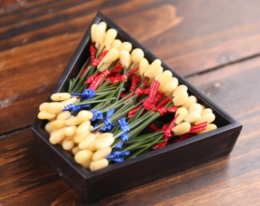 야생에서 채취를 한 잣을 껍질을 깐 후에 솔잎을 꼿아 막대사탕처럼 만든 잣솔을 사다리꼴 모양의 검은 그릇에 수북하게 담아서 마룻바닥에 놓아두고 찍은 사진