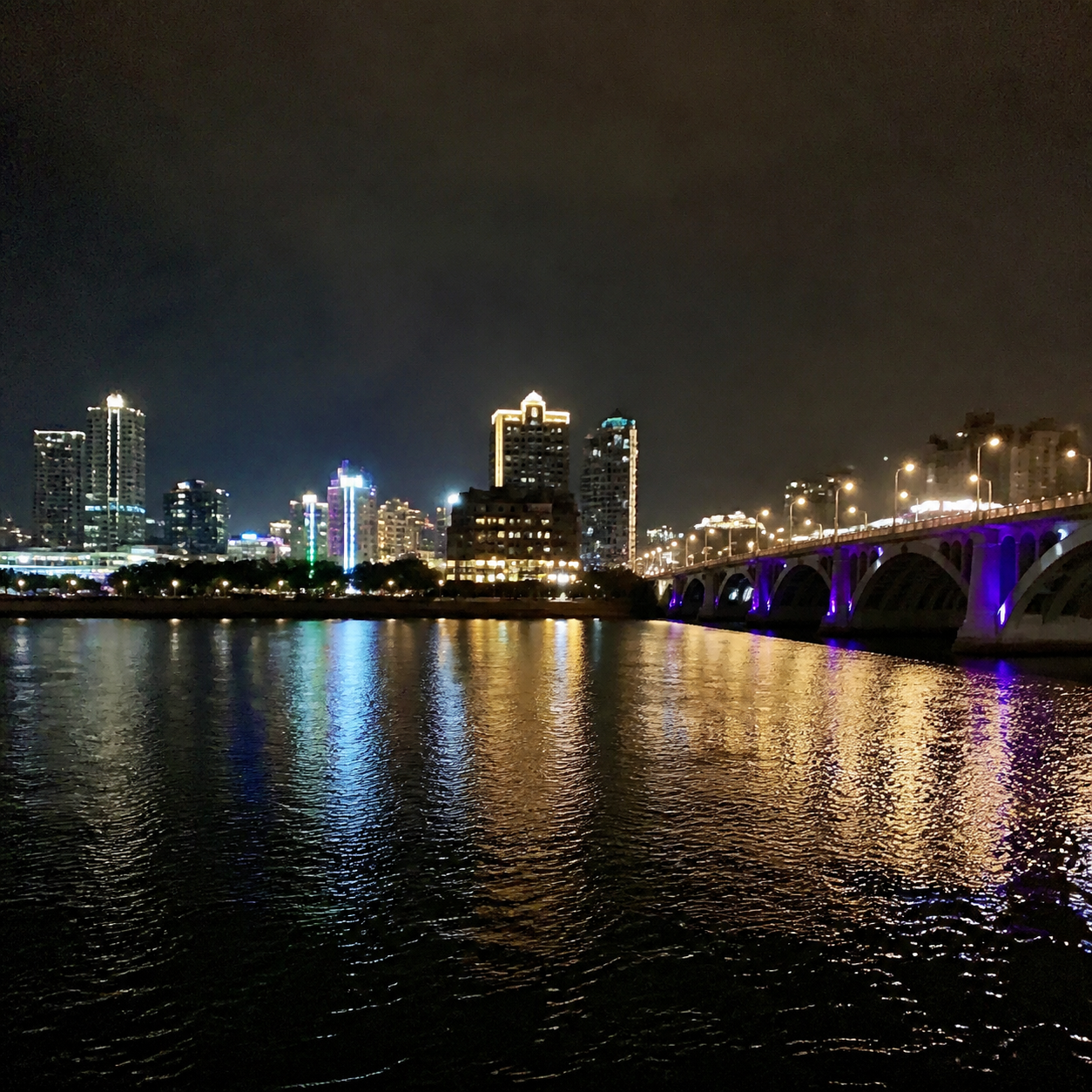 City lights and a lit bridge reflected on dark river water