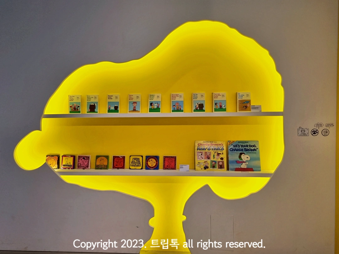 벽에 노란 스누피 형상이 있고 책들이 진열되어있다