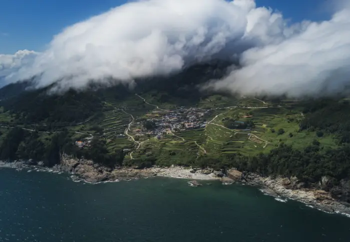 바다를 앞에 두고 계단식 논이 펼쳐진 다랭이 마을 위 구름이 감싸고 있는 모습
