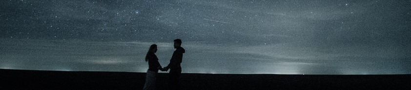 밤하늘에 많은 별들이 떠 있고, 땅에는 행복해 보이는 남녀 한쌍이 양손을 마주 잡고 있는 사진