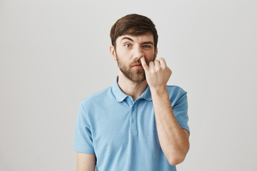 하늘색의 반팔 티셔츠를 입은 서양 남성이 왼쪽 새끼손가락을 이용하여 본인의 왼쪽 콧구멍을 후비고 있는 것을 찍은 사진