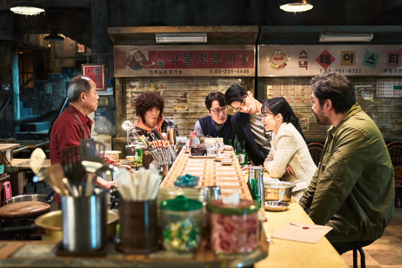 길복순이 여러 킬러들에 둘러싸인 채 식당에서 이야기 하고 있는 모습