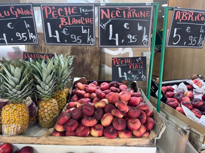 A rustic wooden crate piled high with fresh European donut peaches at a Parisian local market