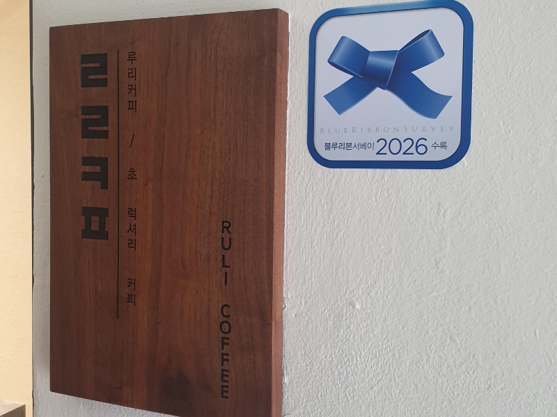 입구에 부착된 블루 리본과 목간판. 목간판에는 ㄹㄹㅋㅍ와 초 럭셔리 커피라는 문구가 있다.