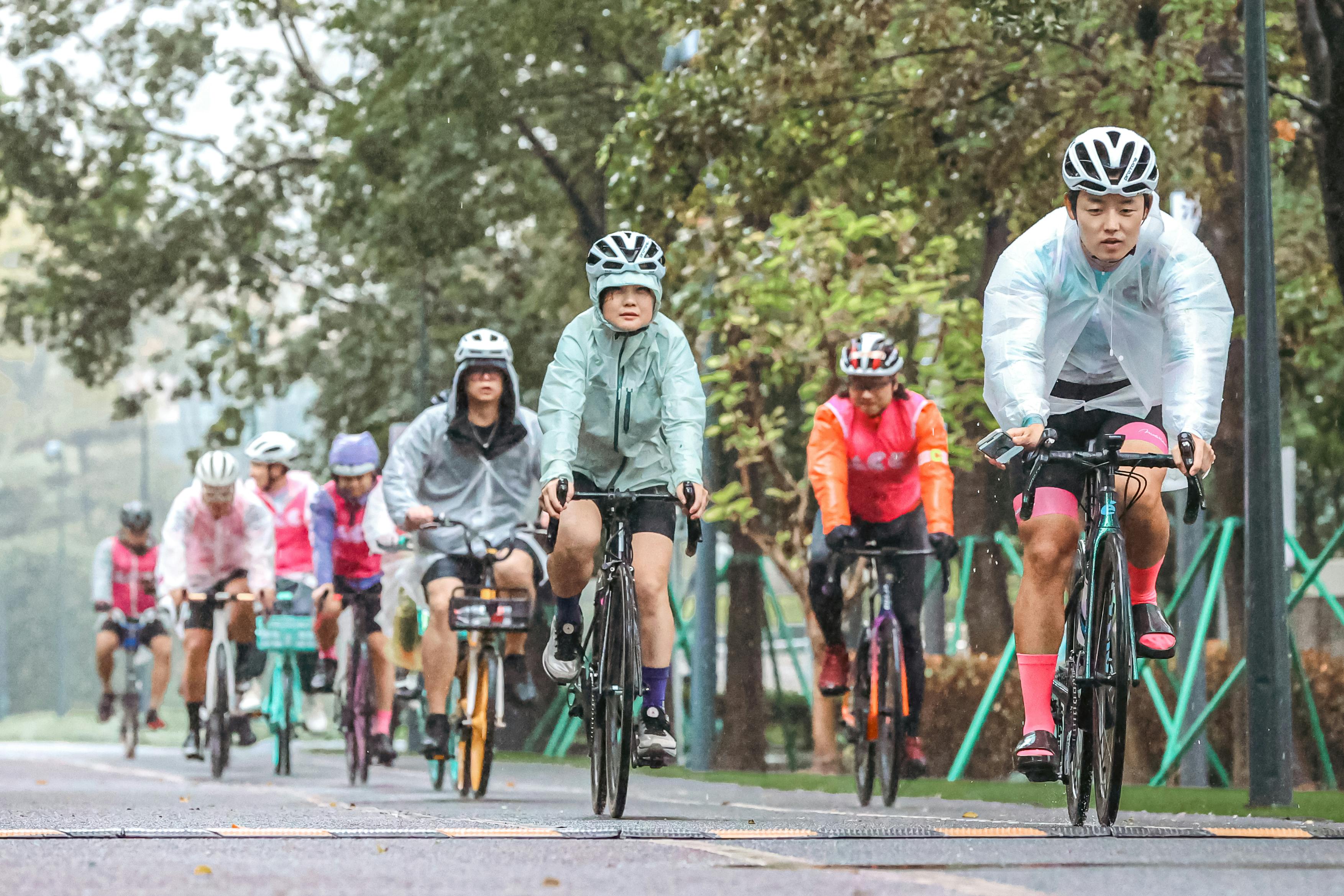 비 오는 날 우비를 입고 도로 위에서 단체 자전거 라이딩을 즐기는 라이더들. 각자 헬멧과 방수 자켓을 착용하고 안전하게 주행 중이다. 젖은 노면과 흐린 날씨 속에서도 질서 있게 주행하는 모습이 인상적이다.