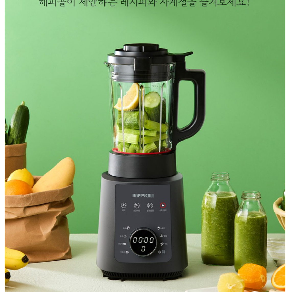 녹색 바탕의 옆에 야채들과 갈아 놓은 쥬스가 담겨있는 병들이 있고, 해피콜 올인원 사계절 초고속 블렌더(HDBL-HAA1GR) 의 본체에 오이와 레몬이 들어 있는 이미지