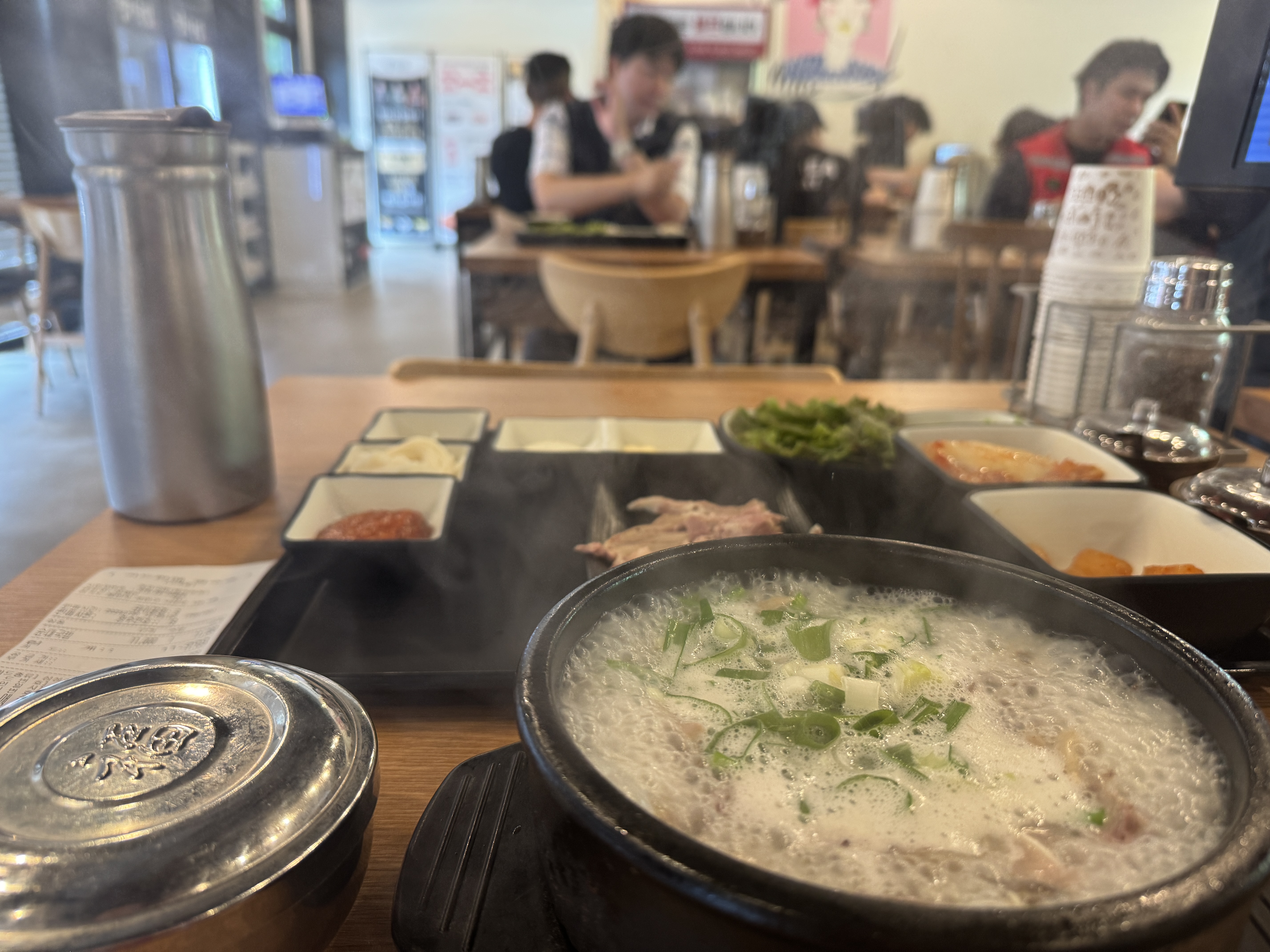 경자국밥 용인본점 테이블 위에 보글보글 끓고 있는 섞어국밥 뚝배기. 송송 썬 파가 올려져 있고, 옆에는 수육과 김치, 깍두기, 쌈채소, 소면, 쌈장 등이 함께 차려져 있다.