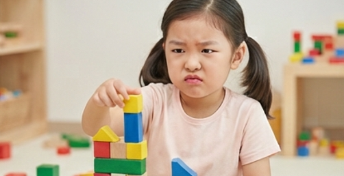 블록이 무너져 속상한 표정으로 다시 쌓는 아이