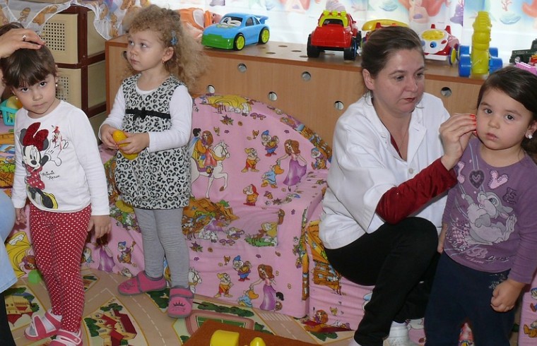 보육교사와 유치원 어린이들이 장난감이 가득한 놀이 공간에서 활동하는 모습. 아동발달지원계좌(디딤씨앗통장) 복지정책의 지원대상 이미지를 상징.