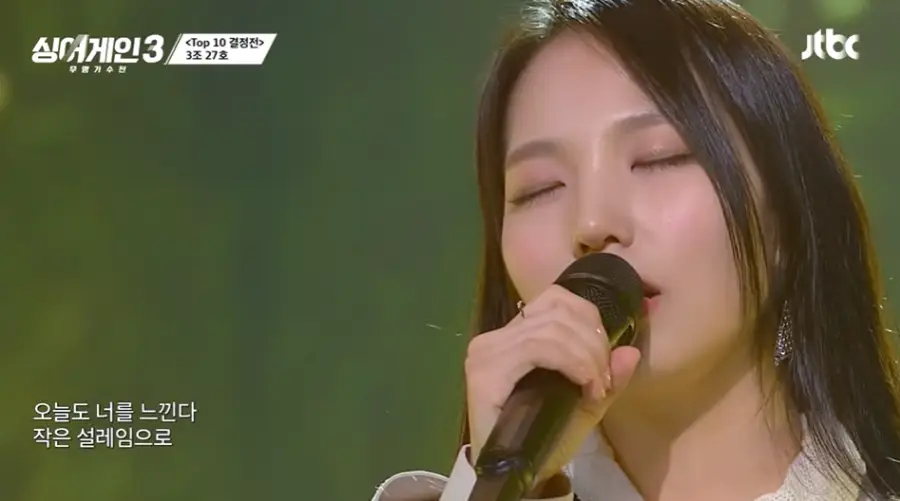 싱어게인3-
초록색 배경 긴머리를 늘어뜨린 27호 여가수가 검은 마이크를 잡고 눈감고서 노래부르는 이미지