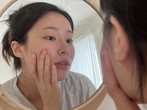 자연광 방 안에서 거울을 보며 팔자주름을 확인하는 20대 여성의 생얼 셀카 느낌 사진