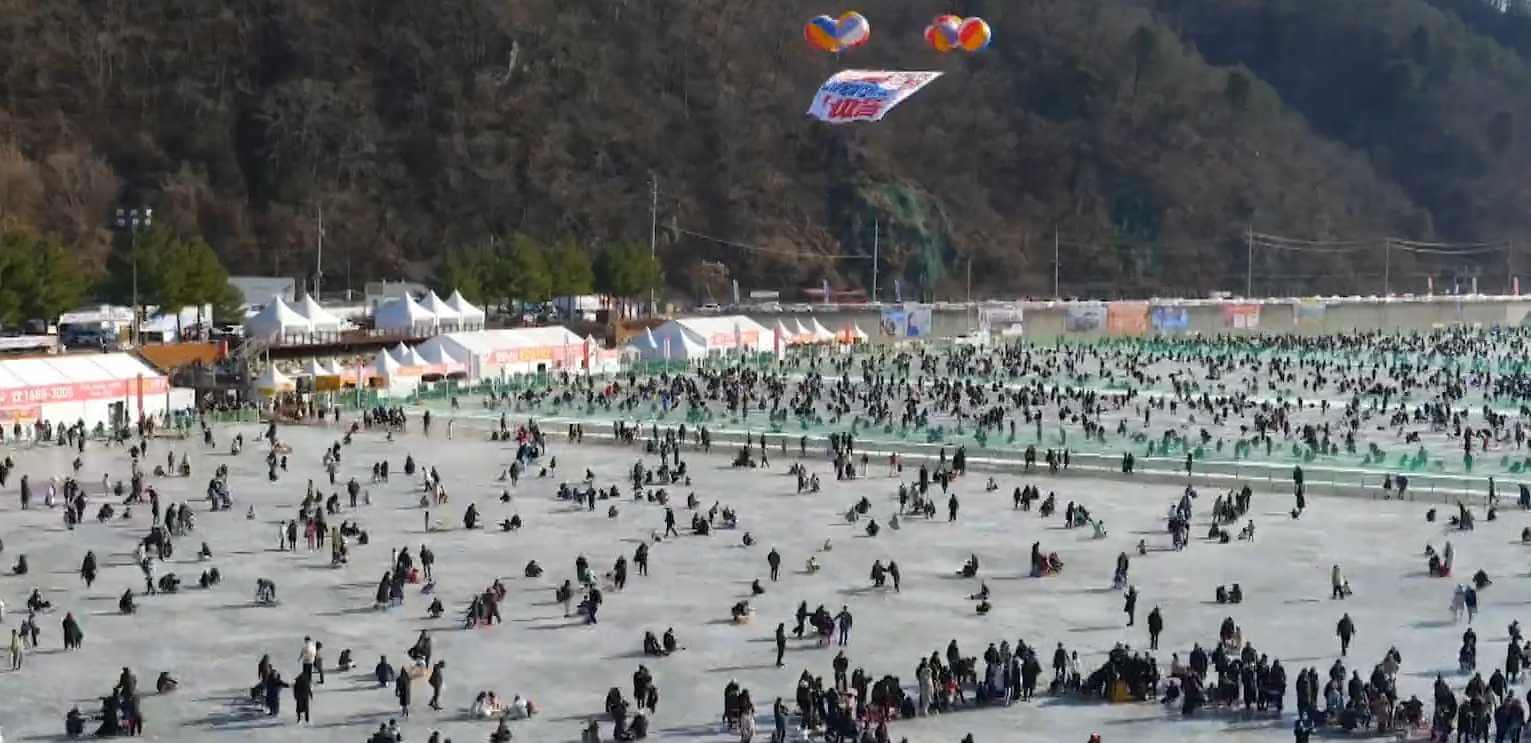 수많은 사람들이 넓은 얼음 위에서 낚시를 즐기는 모습, 축제의 활기찬 분위기를 담은 장면
