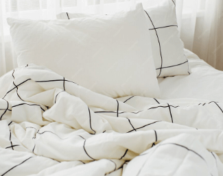 흰색 체크무늬 이불과 베개가 놓인 햇살 드는 침대 위의 깔끔하고 포근한 침구 세트 모습