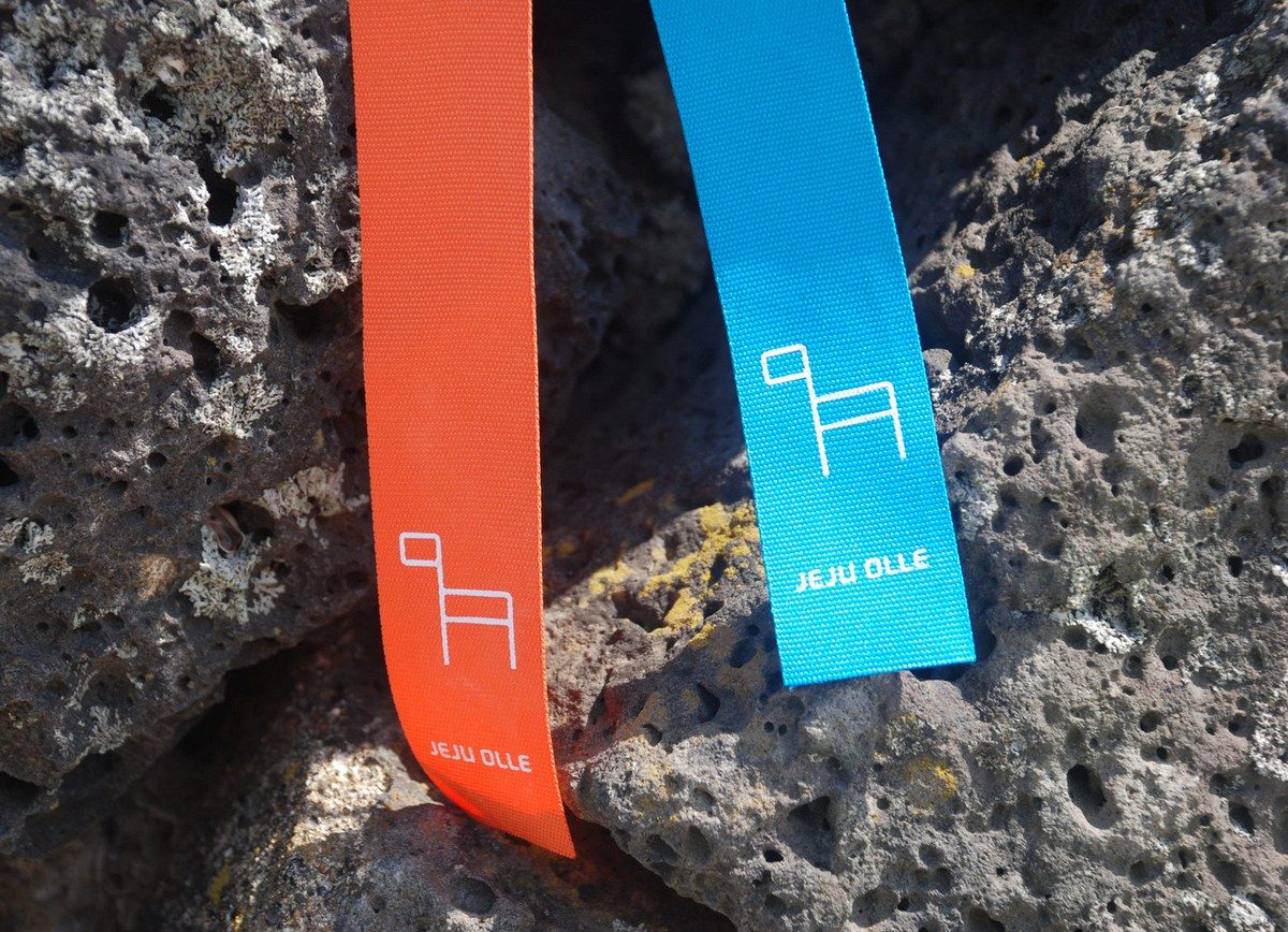 Close-up of orange and blue Jeju Olle ribbons hanging over volcanic rock, the trail markers used to follow Route 19 and Route 20