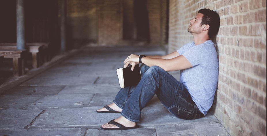 지친듯한 표정을 하고 있는 젊은 남성이 골목에서 벽에 기대어 앉아 있는 사진