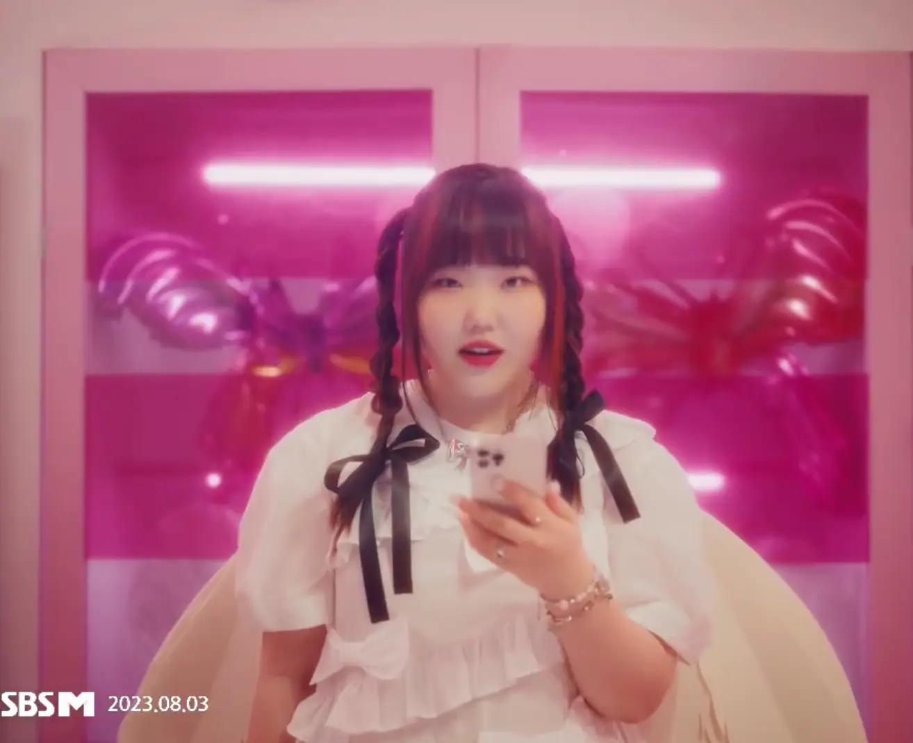 악뮤-분홍색 배경 앞 핸드폰을 들고 노래하는 수현