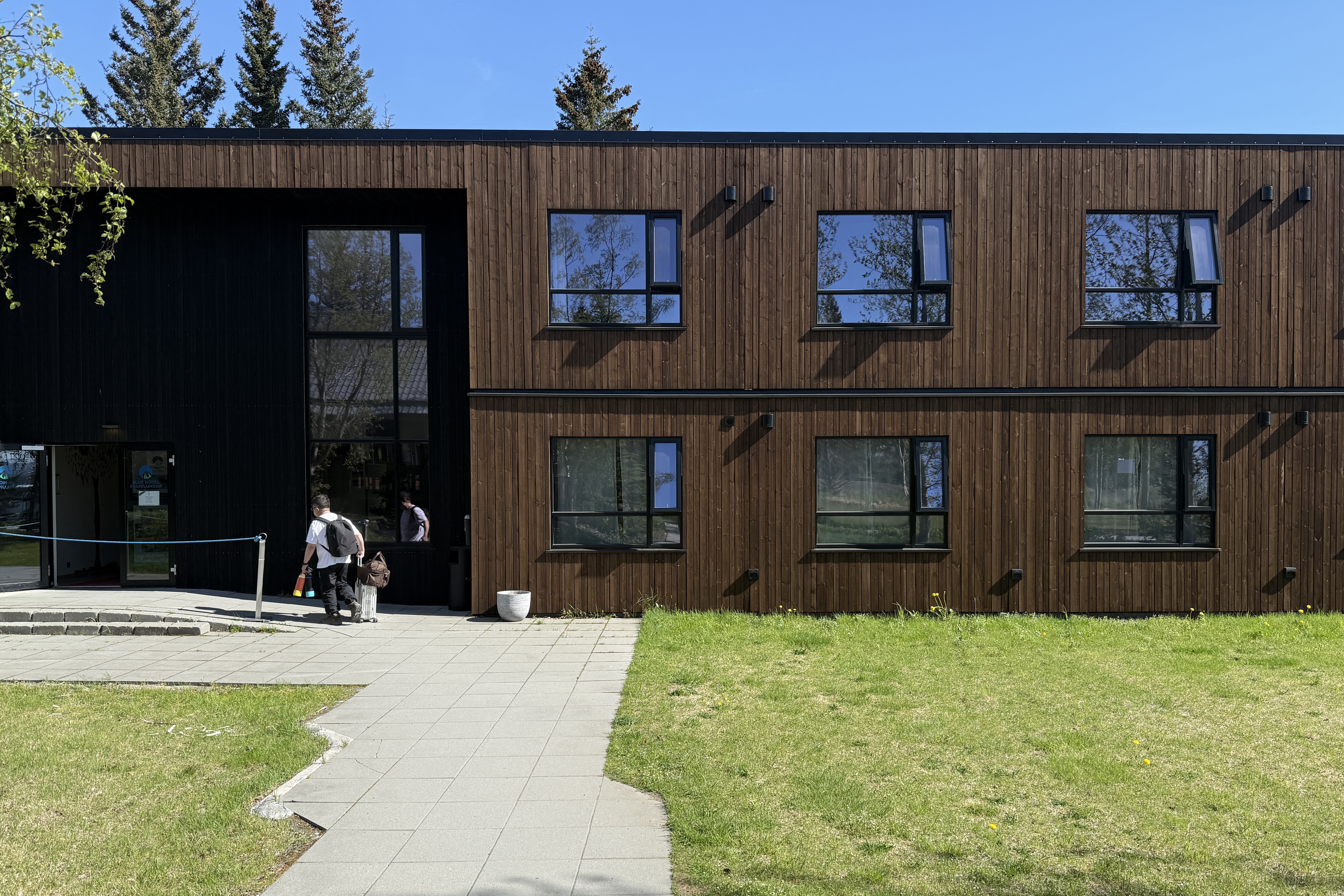 짙은 갈색과 검정색 목재로 지어진 2층짜리 블루호텔 건물 외관, 입구 앞에는 여행객이 건물 내부로 출입중