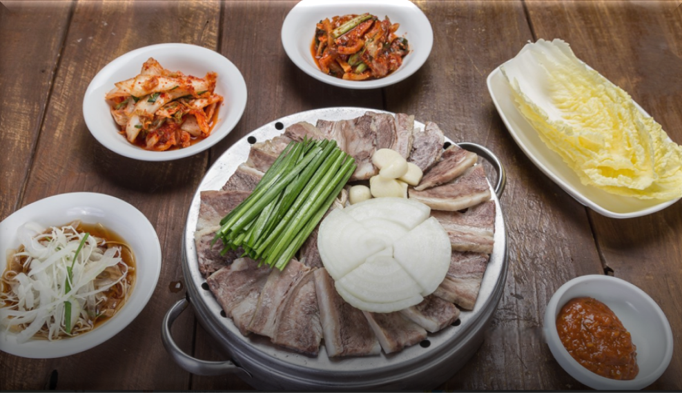 양파와-부추-마늘이-올려진-수육과-알배추,-김치,-무말랭이-등-반찬들이-차려져-있는-특미수육-한상