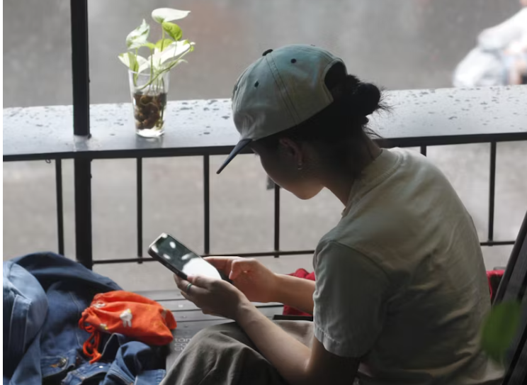 모자를 쓴 여성이 창가에 앉아 스마트폰을 사용하는 모습, 생활 속 앱 활용 장면