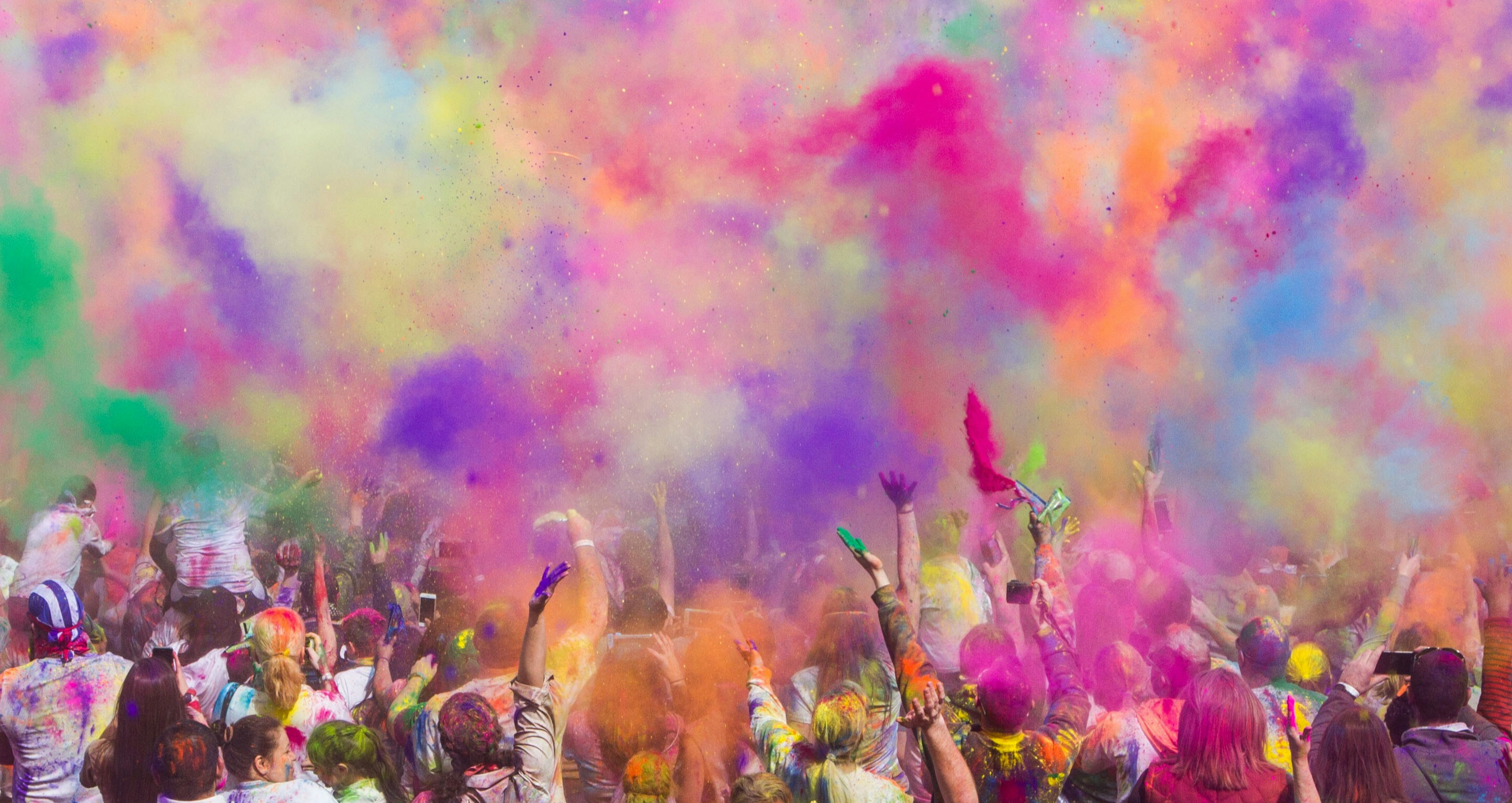 수많은 사람들이 인도 홀리 축제에서 형형색색의 색가루를 뿌리며 즐기는 장면, 하늘에 퍼지는 색가루와 환호하는 군중의 모습