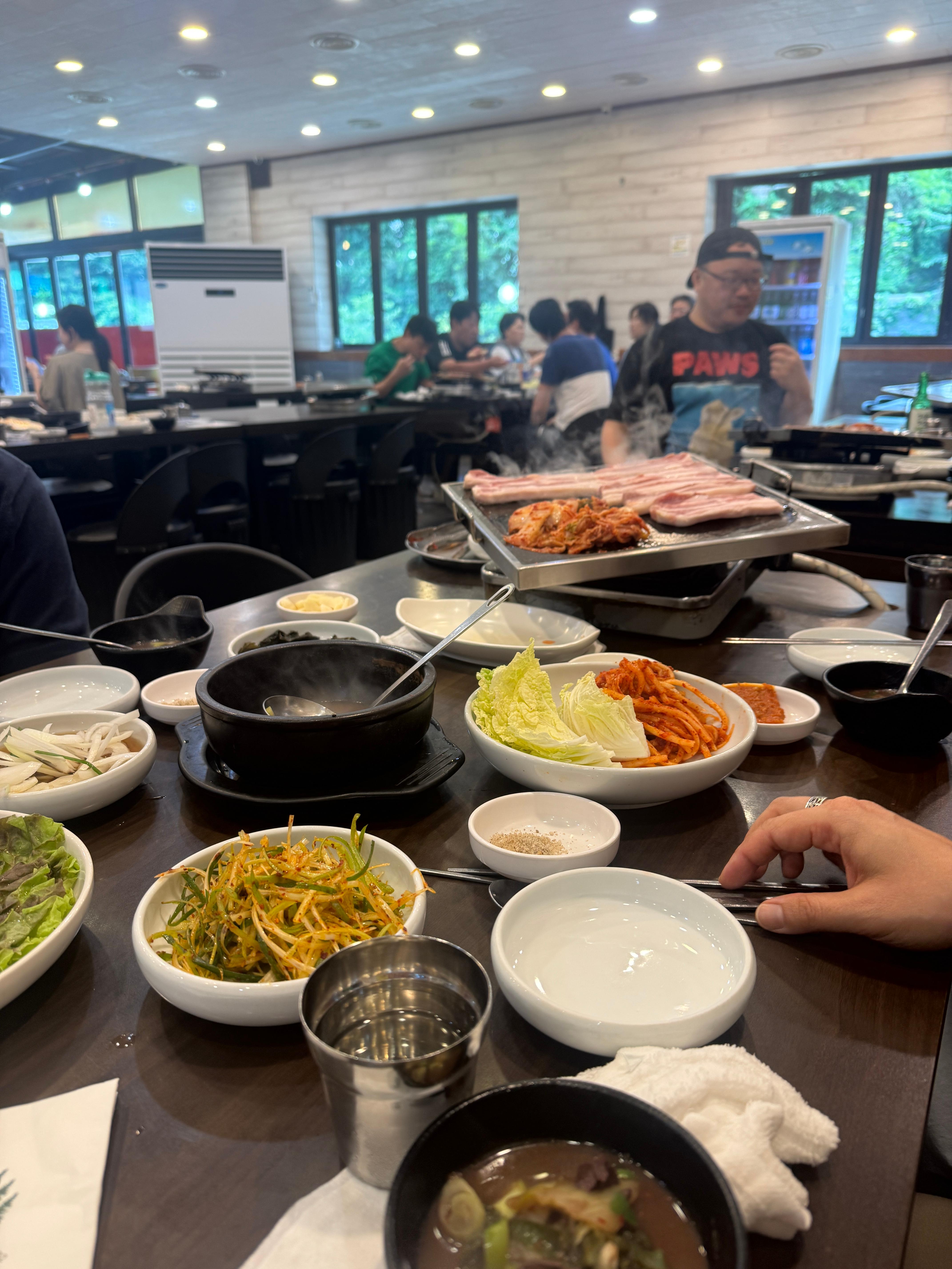 솔밭삼겹살 테이블 한쪽. 돌판 위에 삼겹살과 김치가 구워지고 있고&amp;#44; 밑반찬과 선지해장국이 가지런히 세팅되어 있다.