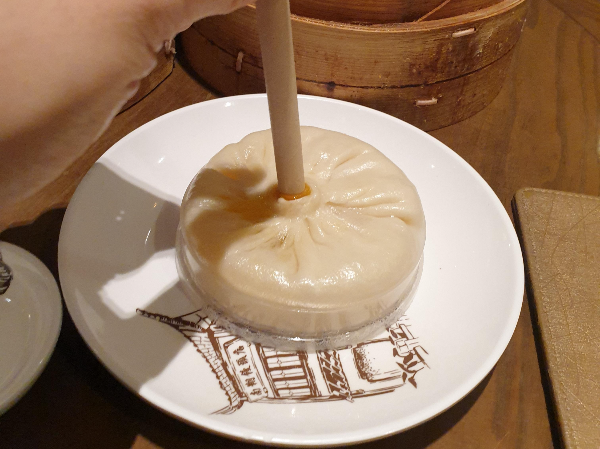 크고 넓은 만두 가운데에 빨대를 꽃아 육즙을 먹는 모습