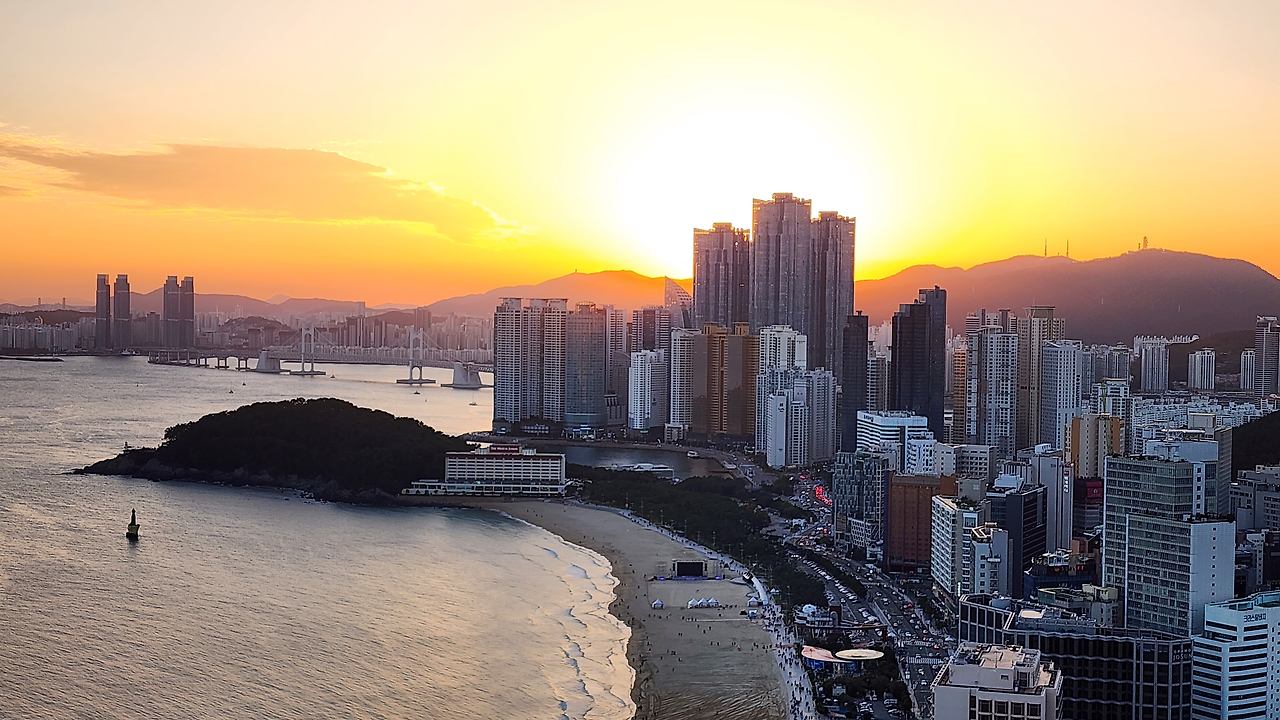 노을이 물든 하늘 아래 고층 빌딩과 해운대 해수욕장이 펼쳐진 풍경, 부산의 상징적인 전경.