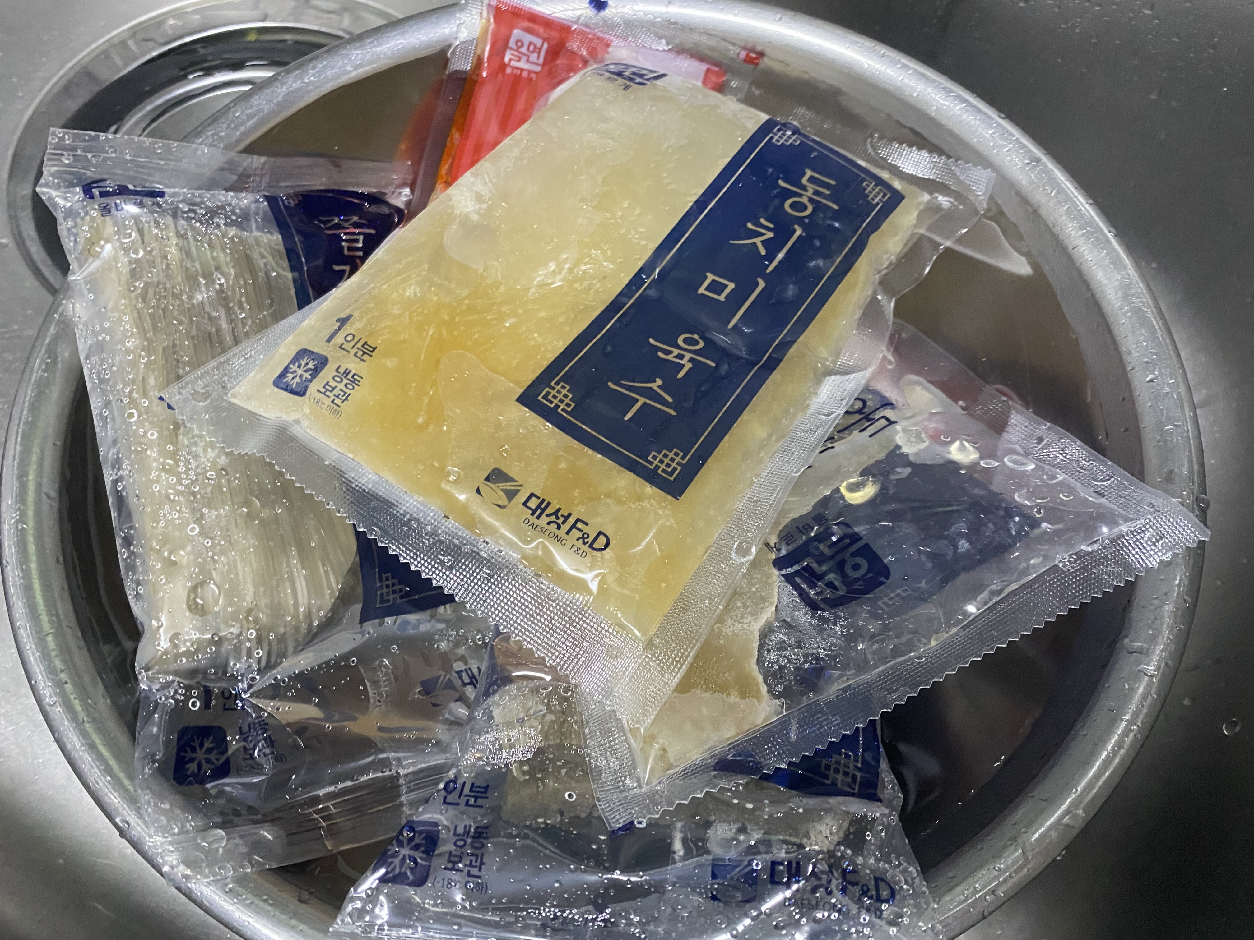 냉면 밀키트를 흐르는 스테인레스 볼에 담아 물에 담궈서 해동하는 사진