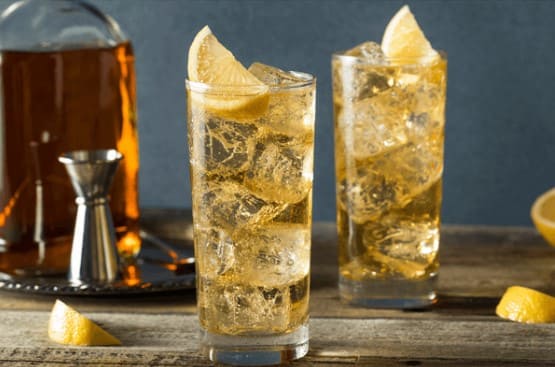 유리잔에 노란색 액체가 들어가 있고 위에 레몬 조각이 올라가 있다.