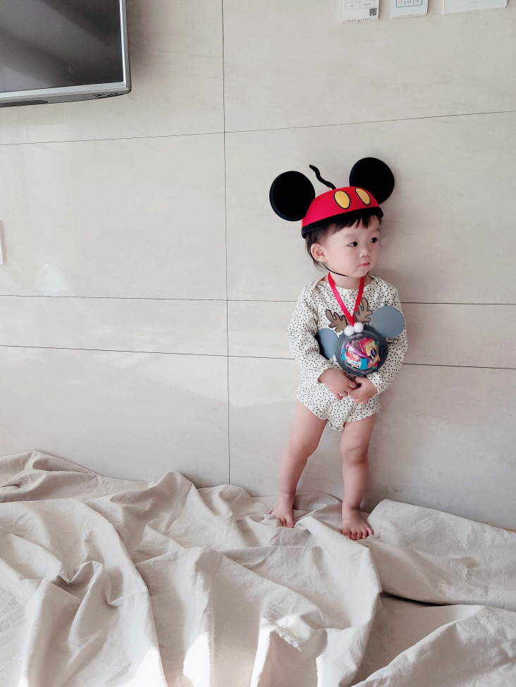 미니마우스 모자에 미니마우스 사탕 목걸이를 목에 걸고 포즈 취하는 아기 모델