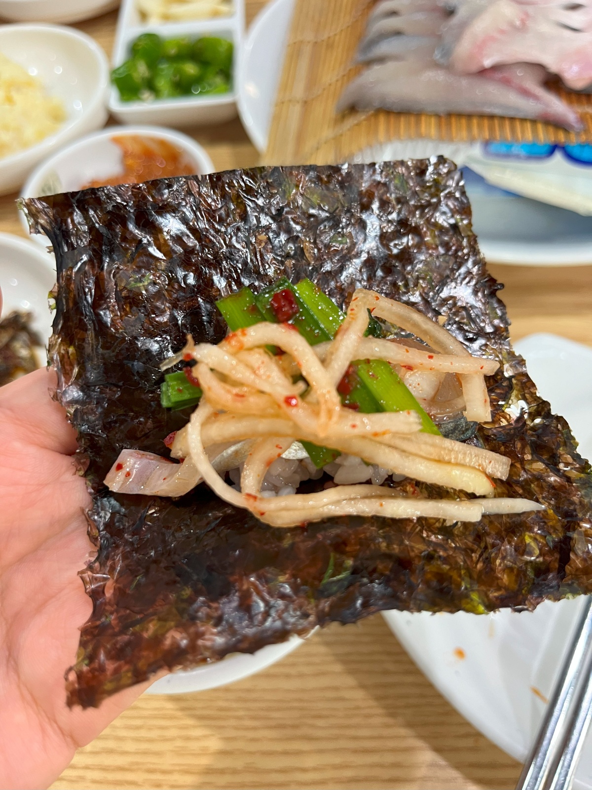 돌김 위에 양념된 밥&amp;#44; 고등어회&amp;#44; 부추&amp;#44; 무생채가 올라가 있다