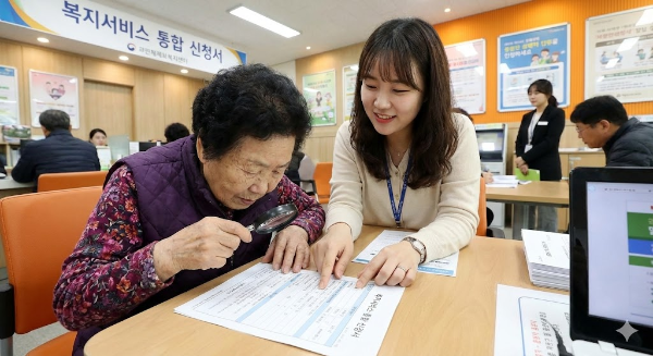 동사무소 창구에서 친절한 공무원의 설명을 들으며 복지카드 신청 서류를 작성하는 어르신