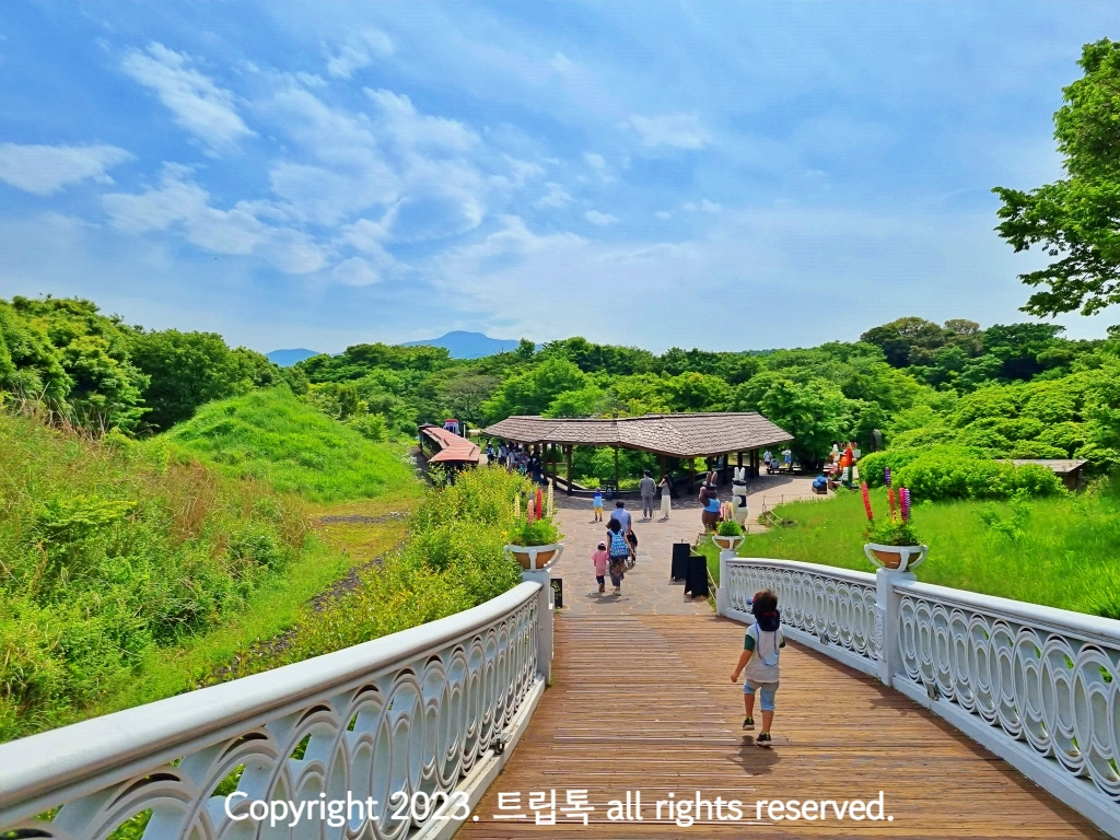 나무로 이루어진 다리를 지나는 아이와 그 앞에 지붕이 있는 벤치에서 족욕을 하는 사람들