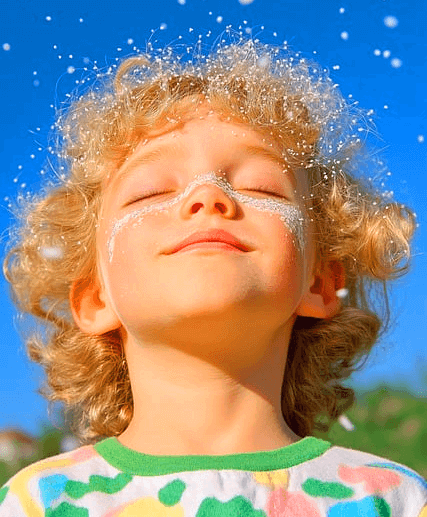 금발 곱슬머리 남자아이가 두 눈을 감은채 하늘 위로 얼굴을 올렸다. 머리 주변에는 하얀 방울들이 가득하다.