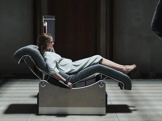 영화 <패러다이스> 속 인물이 수명 거래를 위한 의료 기계 위에 누워 있는 모습. 인간의 생명이 자본 시장의 재화로 전락하여 거래되는 시스템의 비인간적인 단면을 상징함.