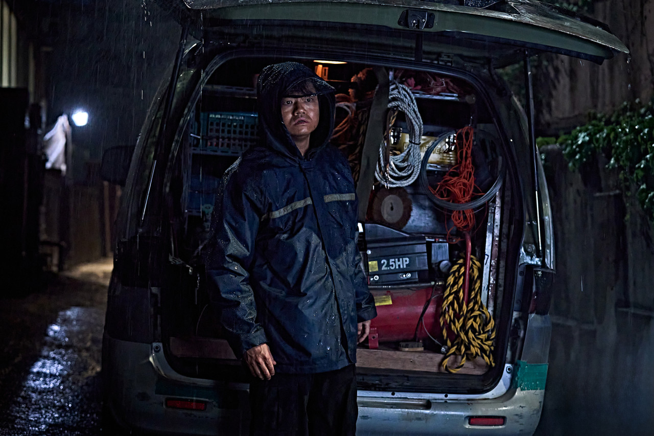 한-남성이-봉고차-트렁크를-열고-정면을-응시하고-있습니다.