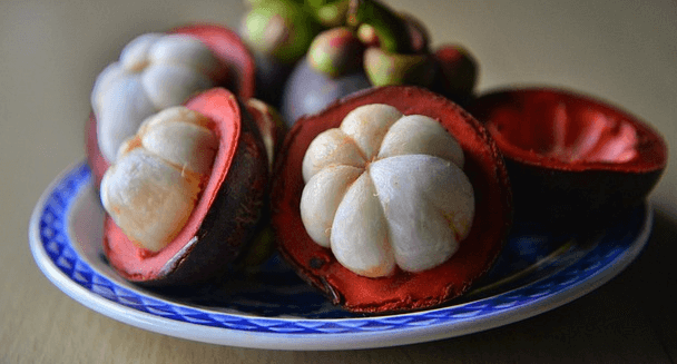 하얀 속살을 반쯤 드러낸 망고스틴의 단면이며 중국식 도자기 접시에 담겨있다.