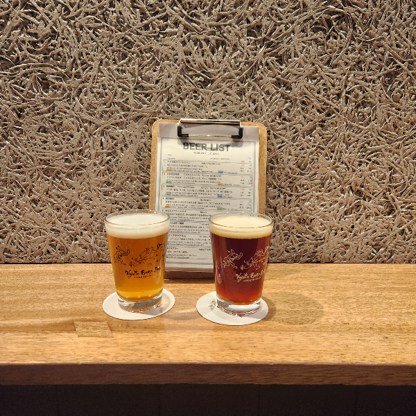 스탠딩 테이블에 맥주 2잔이 올려져 있다. 가운데 메뉴판도 보인다.