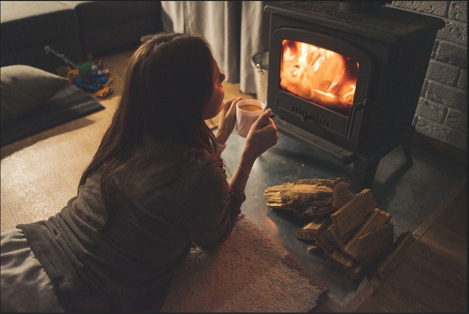 벽난로 안에 장작불이 따뜻하게 타고 있고, 그 앞에서 젊은 여인이 차를 마시고 있는 사진