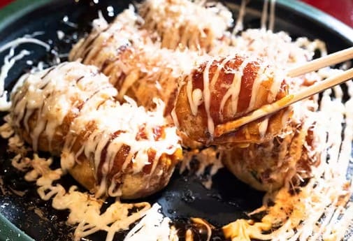 흰색 소스와 갈색 소스가 올라간 동그란 타코야기를 젓가락으로 집고 있다