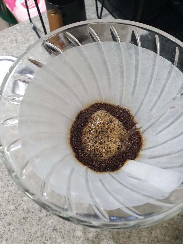 드리퍼 안에 필터가 장착되어 있고 필터에는 이미 물에 젖은 커피 파우더가 있다. 커피 가루에 정확히 푸어 중인 모습