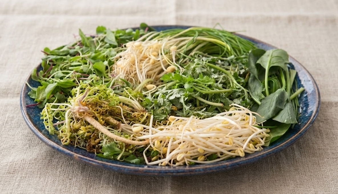 내추럴한 체크무늬 린넨 식탁보 위에 놓인, 묵직하고 단아한 청보랏빛 사기그릇에 가득 담긴 다양한 종류의 신선한 봄나물들. 손질되기 전의 푸릇한 달래, 냉이, 쑥, 미나리, 그리고 숙주나물 등이 다채롭게 어우러진 정갈하고 건강한 식재료 사진.