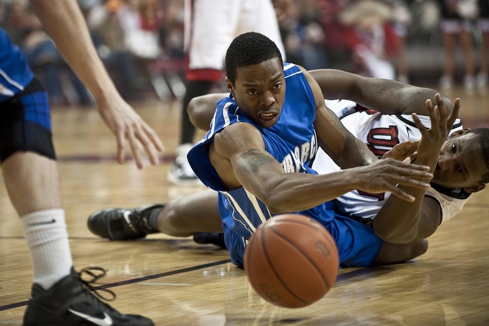Basketball player diving on the court to reach a loose ball during intense gameplay