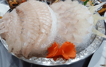 커다란 은색 접시에 하얀색의 광어회가 한가득 담겨있다. 접시 맨앞에는 주황색의 당근으로 만든 당근꽃이 있다.