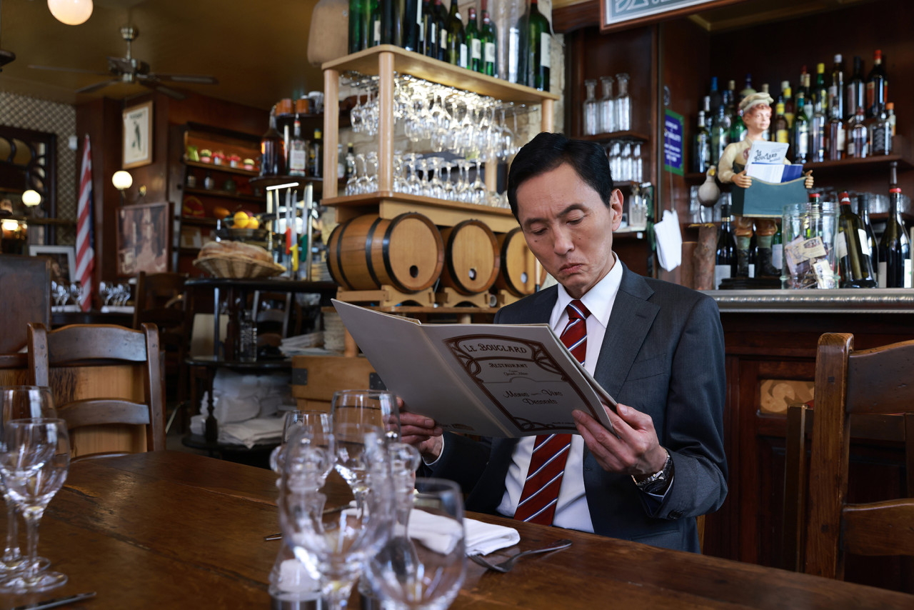 고독한 미식가 더 무비 속 주인공 고로상이 파리 레스토랑에서 메뉴판을 보고 있는 모습