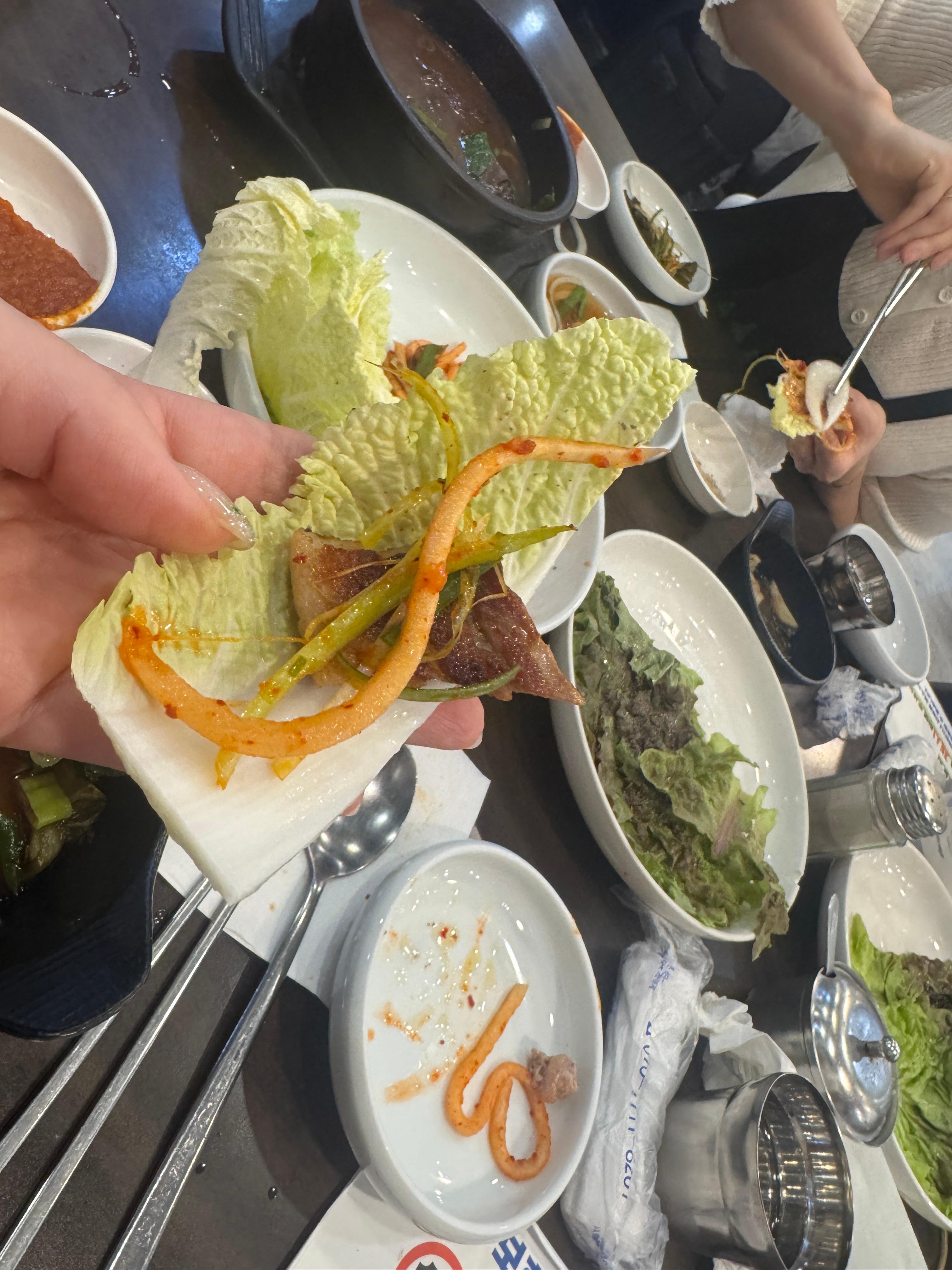 솔밭 삼겹살을 신선한 알배추에 싸서 먹는 장면&amp;#44; 쌈장과 마늘이 곁들여진 모습