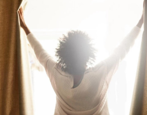 커튼을 활짝 열고 있는 사람의 뒷 모습과 햇살이 들어오고 있는 순간의 사진