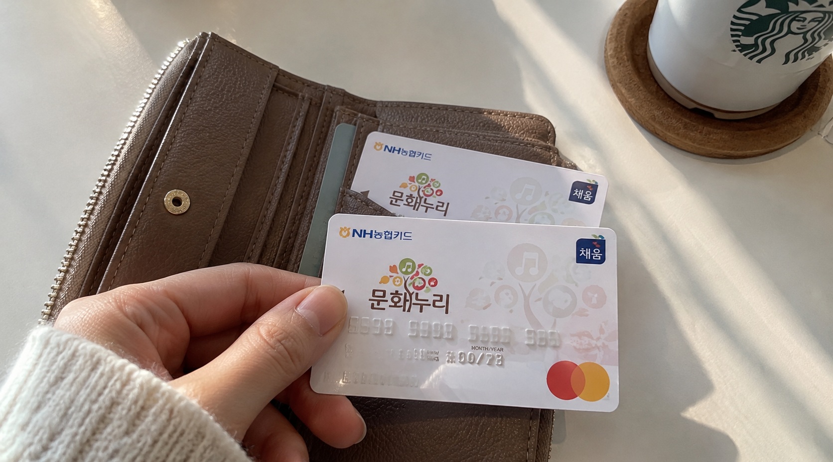 가죽 지갑에서 꺼낸 문화누리카드 실물 2장과 카드 디자인을 보여주는 사진
