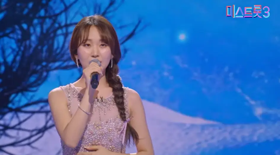 미스트롯3- 파란색 무대비경 보라색 나시 원피스 머리를 왼쪽으로 길게 땋아 오른손으로 마이크를 든채 노래하는 정슬